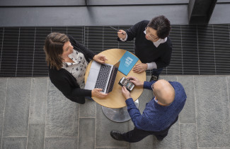 Kolme henkilöä neuvottelee pöydän ympärillä.
