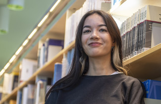 Nainen valaistun kirjahyllyn vierellä.