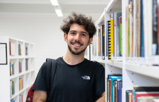 Young man standing between library book shelves.