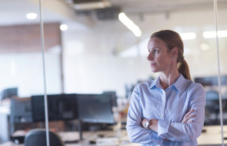 Nainen seisoo toimistossa ja katsoo sivuun kamerasta
