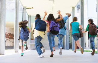 koululaiset juoksevat koulun käytävällä reput selässä