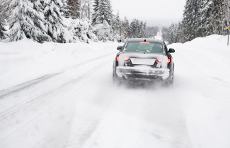 Auto ajaa lumisella tiellä.
