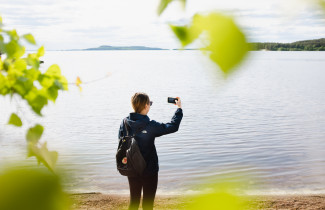 Henkilö kuvaa puhelimella höytiäisen rannalla maisemia. 
