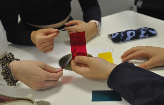 Kuvassa lasten käsiä, kun he ovat kokeilemassa erilaisia värifilttereitä tutkiessaan, kuinka valo käyttäytyy heijastuessaan CD-levyn pinnasta.