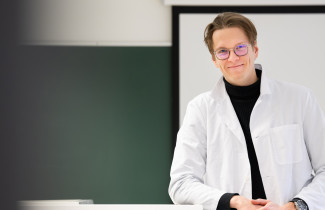 aineenopettajaopiskelija luokkahuoneen edessä laboratoriotakki yllään