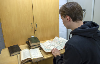 Mies tutkii pöydän ääressä vanhoja kirjoja. A man studying old books at a table.