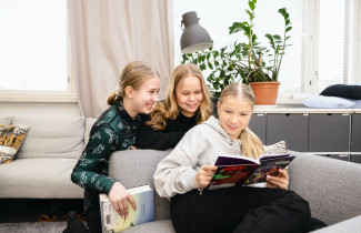 Kolme tyttöä lukee yhdessä kirjaa oppitunnilla.