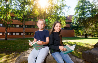 Alakoulun oppilaat ulkona lukemassa kirjaa.