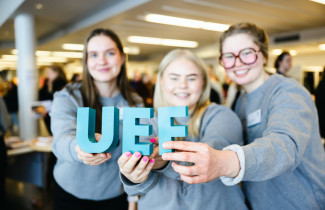 Kolme henkilöä pitää sormissaan UEF-kirjaimia.