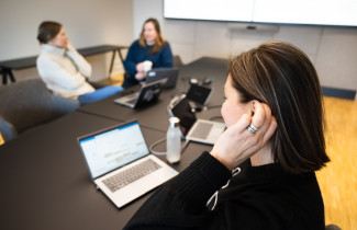 Kokouksen osallistuja koskettaa kuulolaitetta.