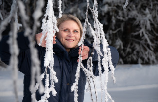 Opiskelija Tanja Nikkilä kurkkaamassa huurteisten oksien välistä talvisessa maisemassa
