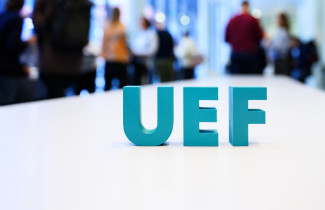 UEF-kirjaimet pöydällä. Taustalla ihmisiä.