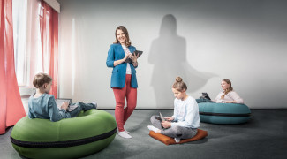 Naisopettaja luokan edessä, varjokuvass opettajalla näyttää olevan supersankarin viitta