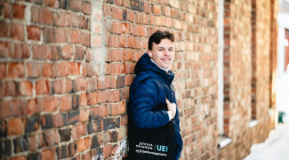 Mies nojaa seinään ja hymyilee kameralle talvella