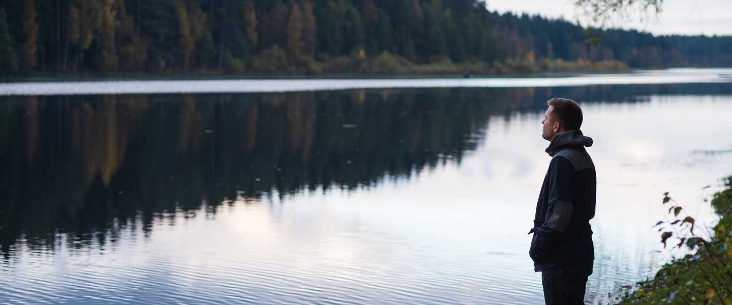 Yksinäinen mies seisoo järven rannalla.