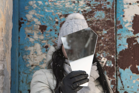 Henkilö pitää peilin palaa kasvojensa edessä