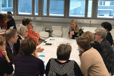 Ihmisiä istumassa pöydän ympärillä tekemässä ryhmätyötä.