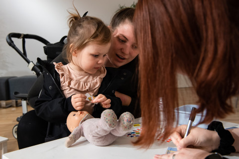 Nainen ja pieni lapsi käyttämässä pehmolelua nallesairaalassa.