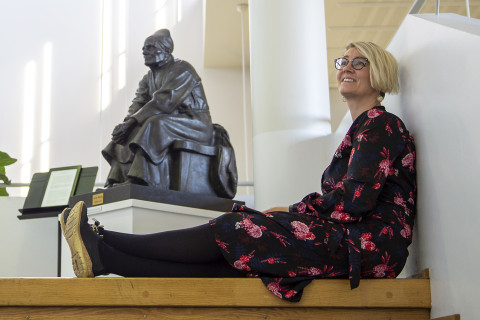 Nainen istuu lattialla runonlaulaja-patsaan vierellä.