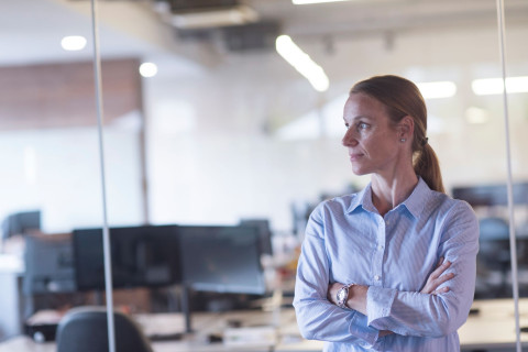 Nainen seisoo toimistossa ja katsoo sivuun kamerasta