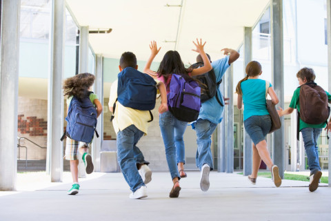 koululaiset juoksevat koulun käytävällä reput selässä