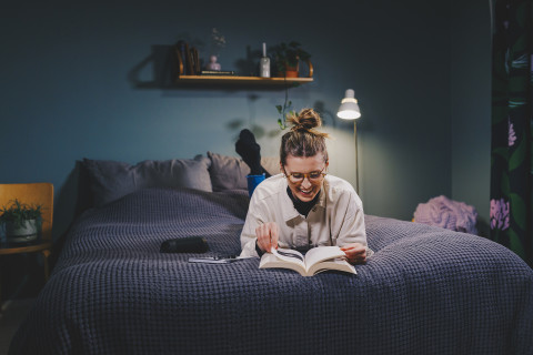 Nainen lukee kirjaa sängyllä maaten