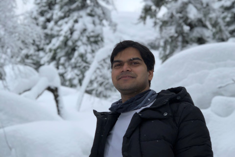 Young man outdoors, looking at the camera smiling, forest covered with white snow behind him.