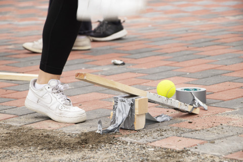 Lähikuvassa katapultti, joka sinkoaa keltaisen tennispallon kohti taivaita