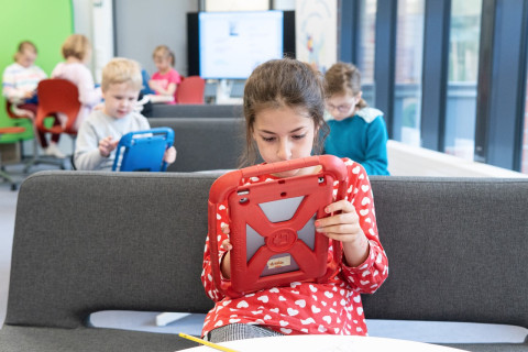 Tyttö istuu koulun sohvalla ja käyttää iPadia.