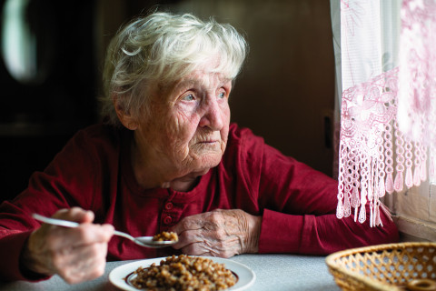 Elderly woman eats sitting at the table.