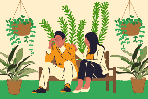 Kaksi henkilöä istuu penkillä viherkasvien ympäröimänä. Henkilöistä toinen peittää kasvojaan käsiin ja toinen pitää kättään toisen olkapäällä.