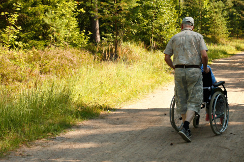 Mies työntää pyörätuolia hiekkatiellä.