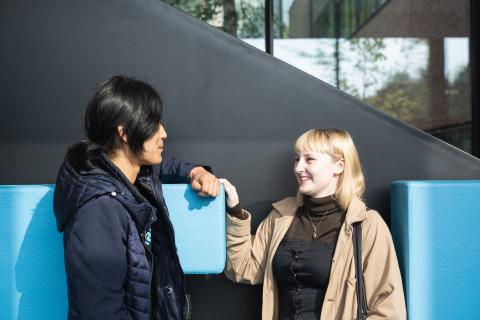 Kaksi opiskelijaa juttelemassa Aurora-rakennuksen portaiden edessä