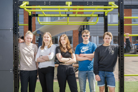 Viisi oppilasta ryhmäkuvassa koulun pihalla.