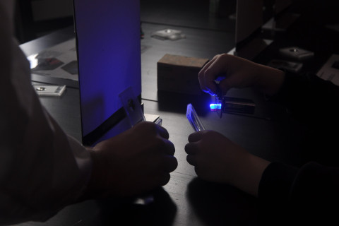 Kuvassa kahden henkilön kädet, kun he tutkivat, kuinka valo käyttäytyy heijastuessaan esineen pinnasta.