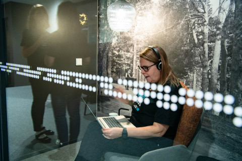 Nainen käyttää tietokonetta kuulokkeet päässä.