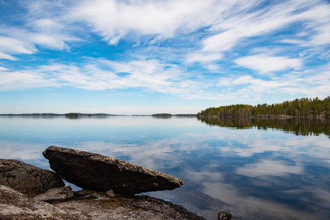 Järvi, kiviä, metsää ja pilvinen taivas.