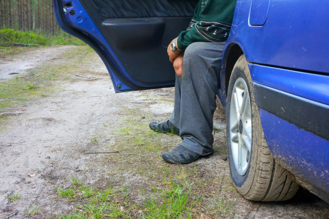 Henkilö istuu auton etupenkillä jalat auton ulkopuolella.