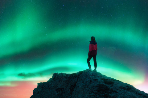 Henkilö katsomassa kukkulalla revontulia.