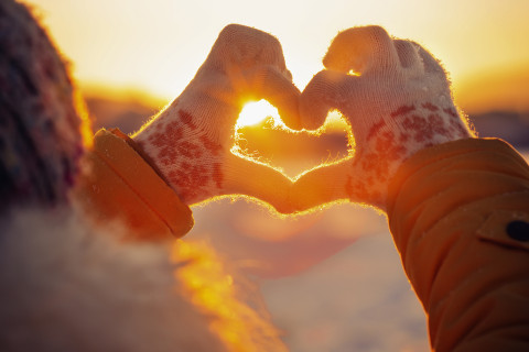 Kädet muodostavat sydämen auringonvaloa vasten talvella.