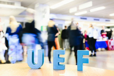 UEF -kirjaimet pöydällä taustallaan Hae yliopistoon -päivien ihmisvirtaa