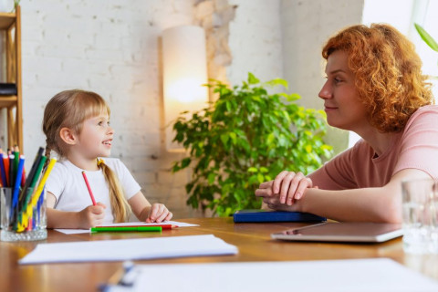 Aikuinen ammattilainen kommunikoi lapsen kanssa pöydän ääressä