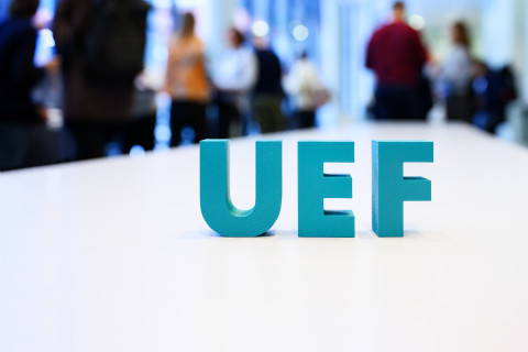 UEF-kirjaimet pöydällä. Taustalla ihmisiä.