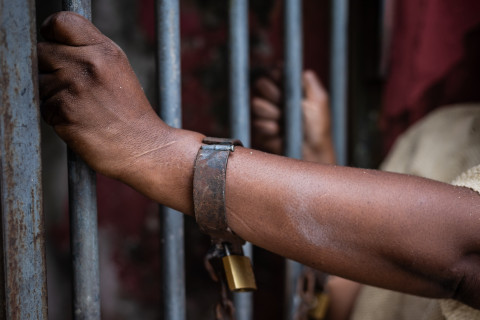 Handcuffs on a person's hand and hands on bars.