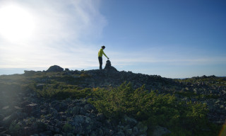 Retkeilijä asettelee kiviä tunturin laella.