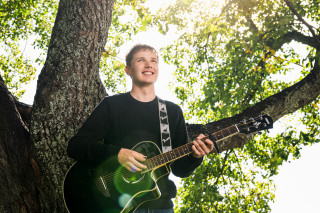 UEF-lähettiläs Konsta Kinnunen kitara kädessä puun alla