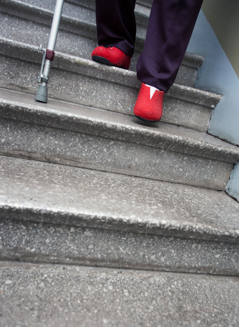 Old person coming down the stairs assisted by a cane.