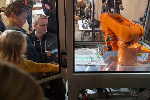 Kolme nuorta katsomassa virtuaalisen konepajan robottia.
