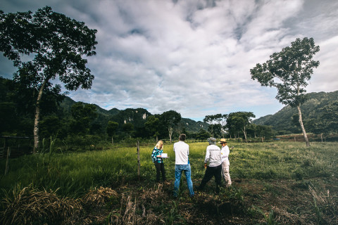 Four people standing on a green field surrounded by hills