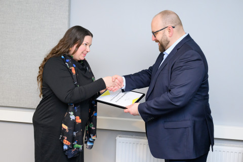 Kaksi henkilöä kättelee palkinnonluovutuksessa.